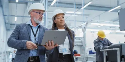 A woman and a man in hardhats looking at a laptop in a manufacturing environment 